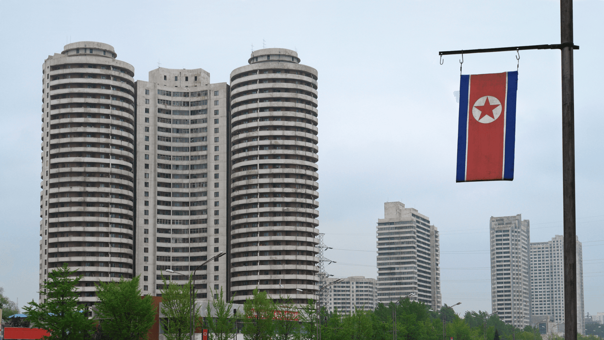 north korea with the flag hanging on the right and some buildings on the left and behind