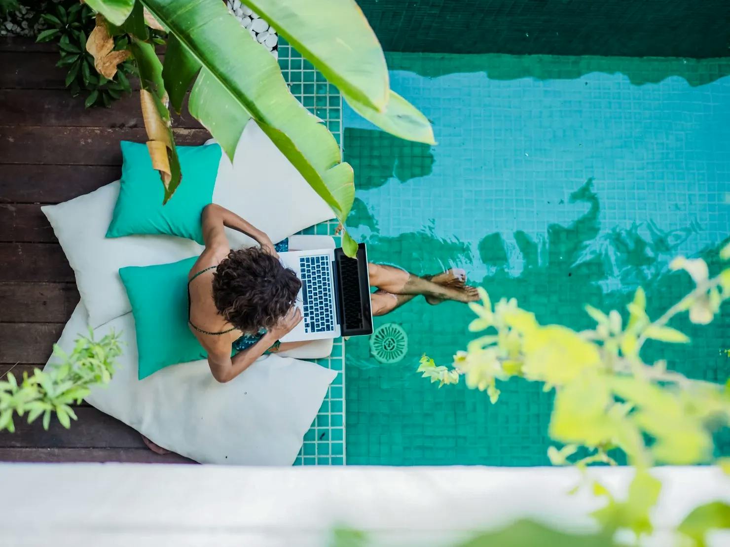 Remote online working digital nomad woman with laptop sitting at a sunny pool