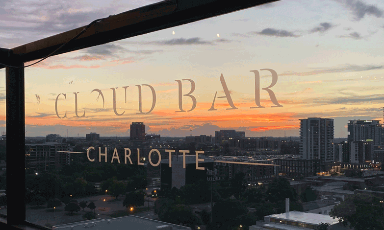 A glass with cloud bar charlotte written on it with the view of sunset