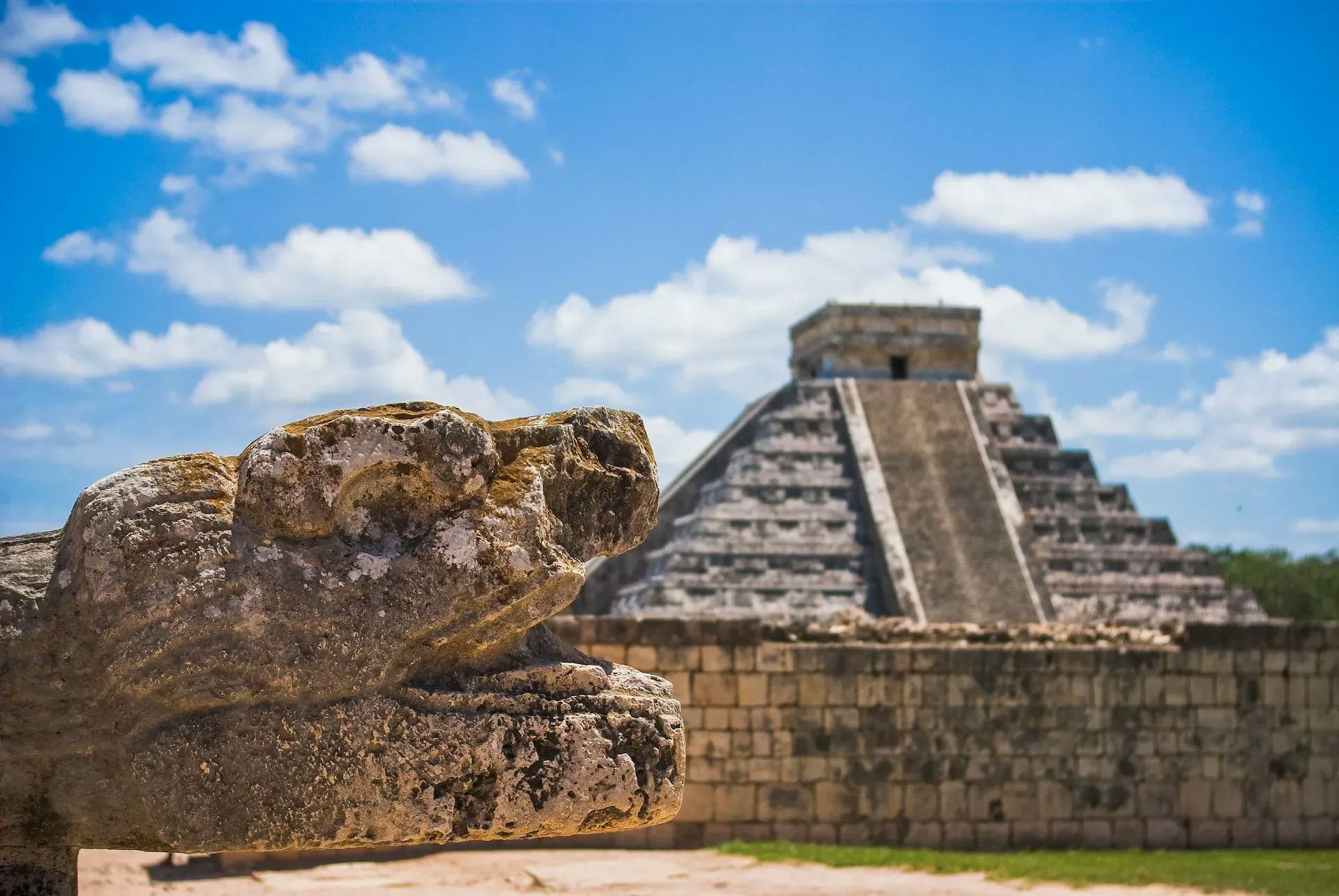 animal head sculpture on the left and the pyramid on the right in chichen itza
