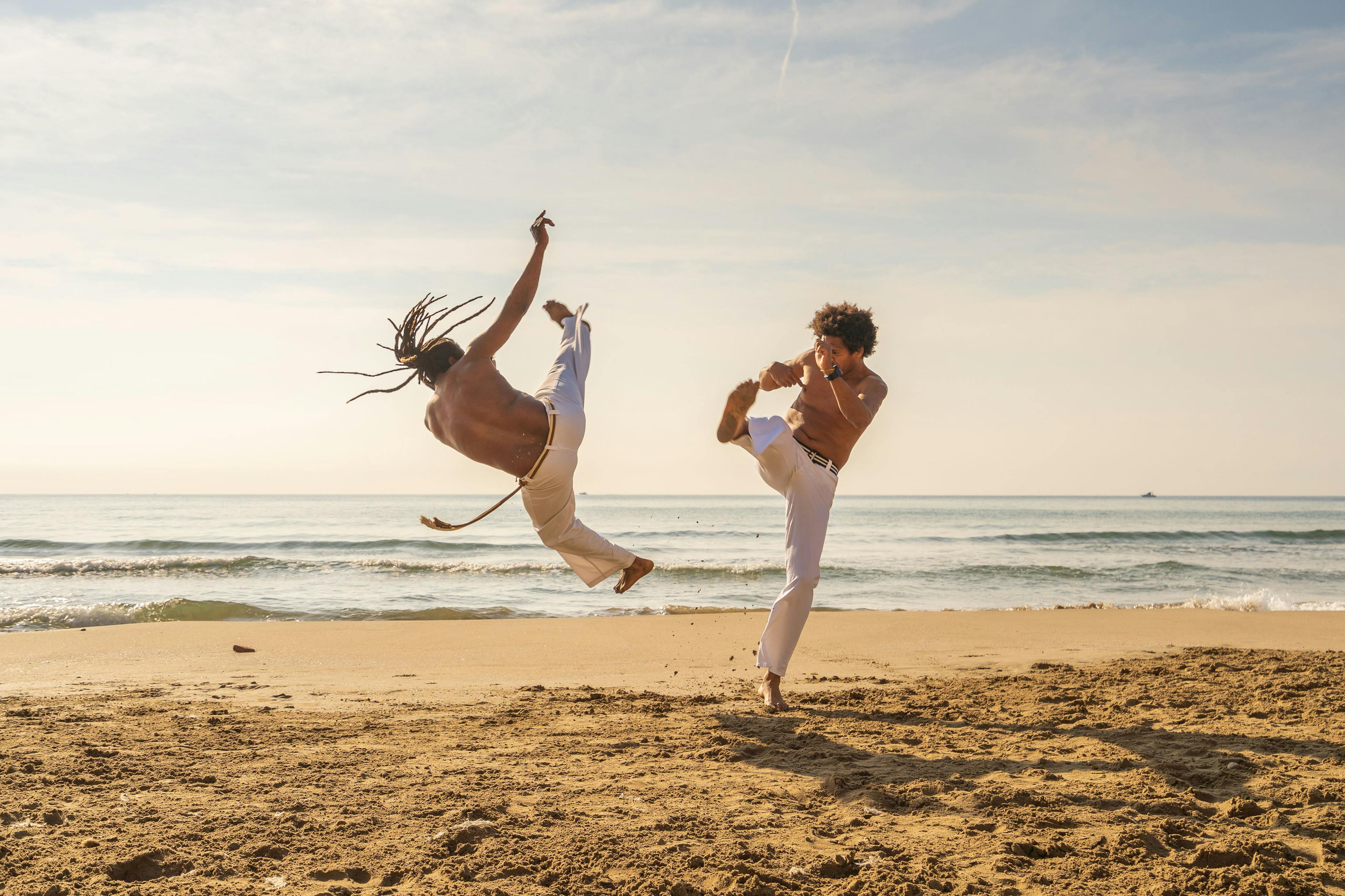 Men train capoeira on the beach