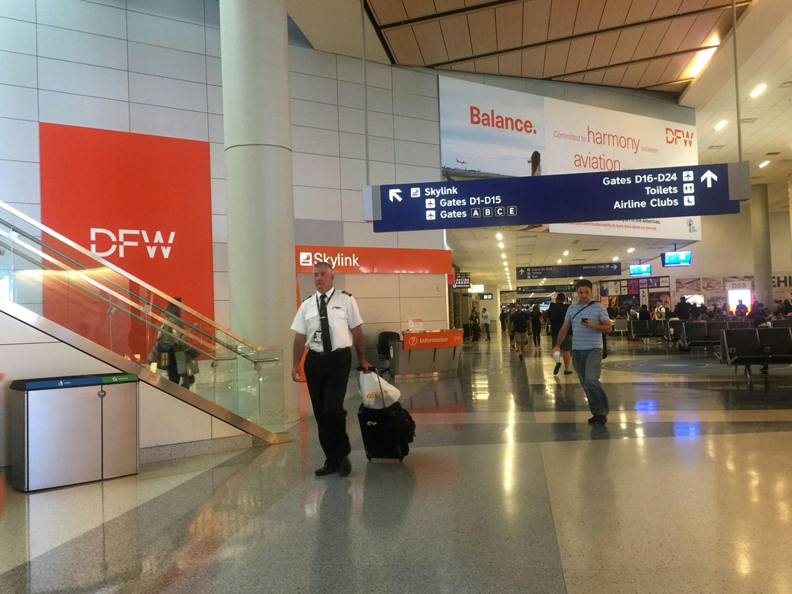 An airplane captain wearing a uniform and carrying a suitcase walks in the terminal of Dallas Fort Worth International Airport